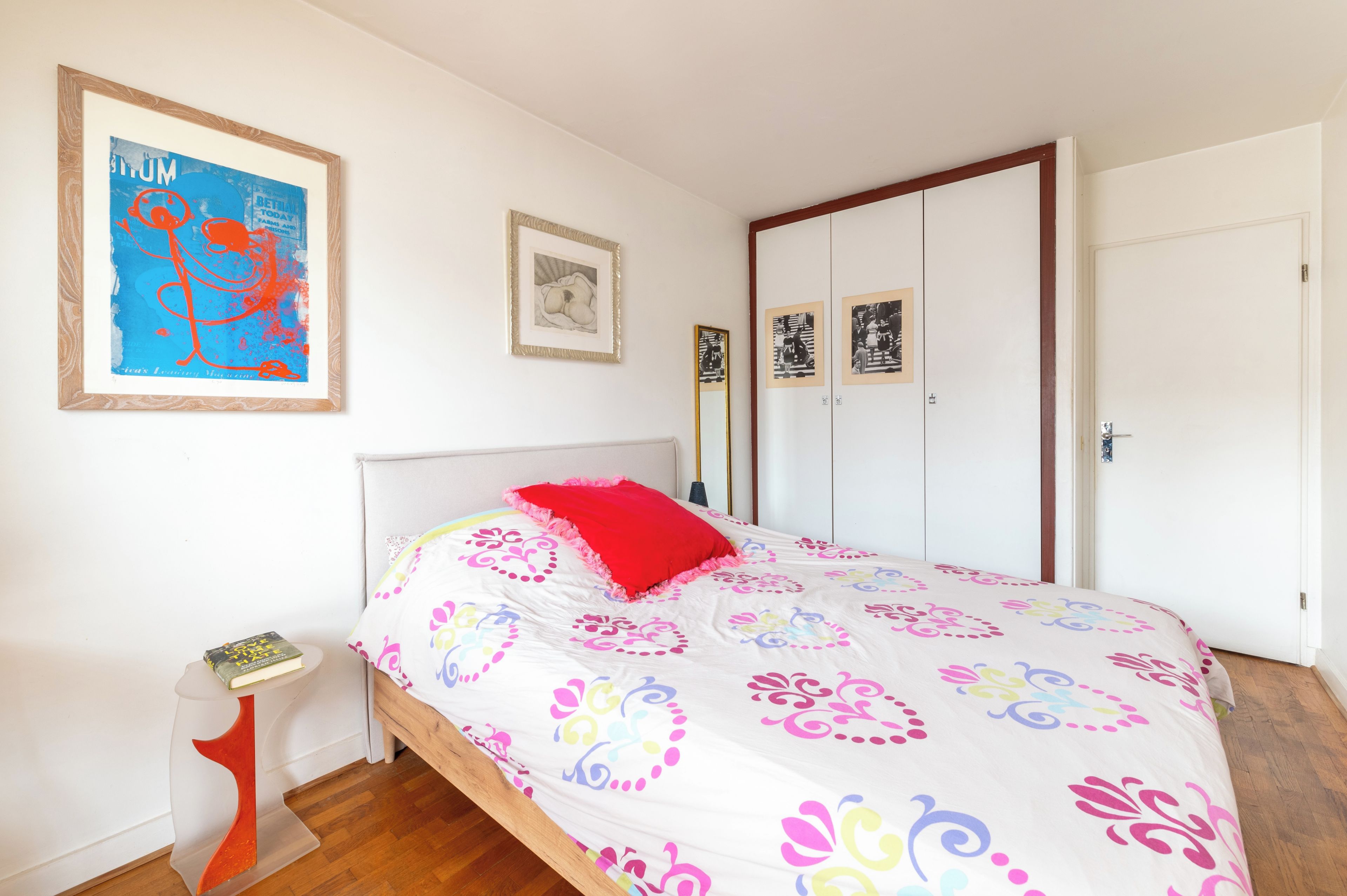 Une chambre à coucher avec un lit, une table de chevet, un tableau encadré, une armoire et une porte.