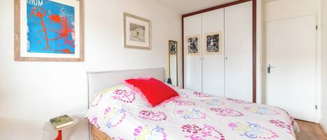 Une chambre à coucher avec un lit, une table de chevet, un tableau encadré, une armoire et une porte.
