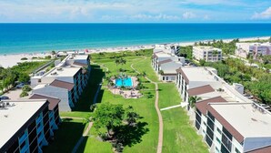 Un resort con varias edificaciones, piscina central y vista al mar.