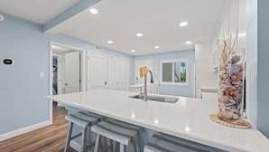 Una cocina moderna con una isla grande, taburetes de bar, un lavamanos y un jarrón decorativo con conchas.