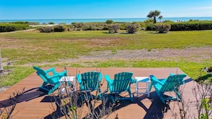 Una terraza con cuatro sillas Adirondack turquesas y una mesita, con vistas a un espacio verde y al océano.