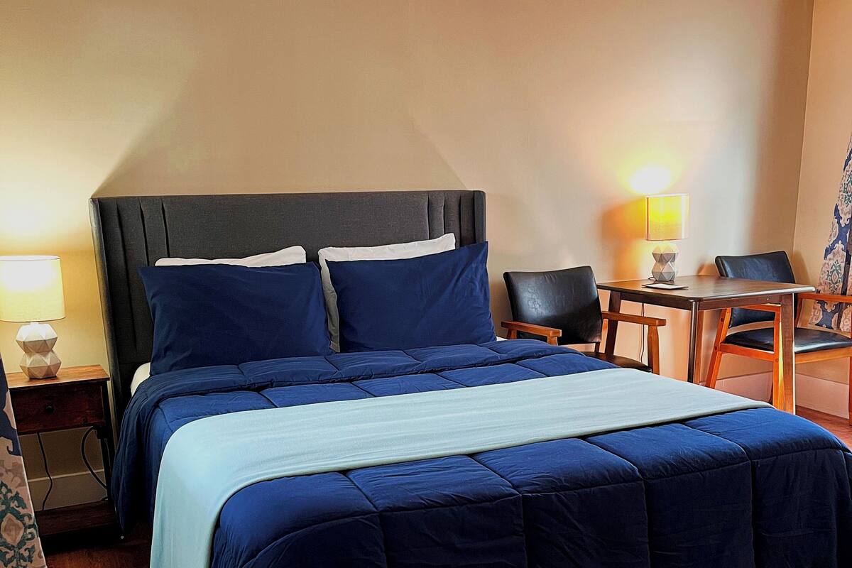 A hotel room with a large bed, a desk, two chairs, and a lamp.
