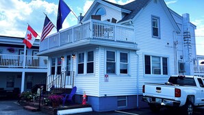 Un bâtiment blanc doté d’un balcon, un camion garé devant et des drapeaux sur le toit.