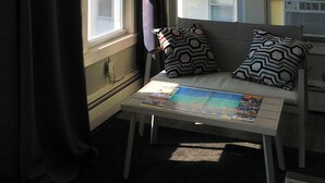 Une petite pièce avec une fenêtre, une table sur laquelle repose un magazine et un canapé agrémenté de coussins à motifs.