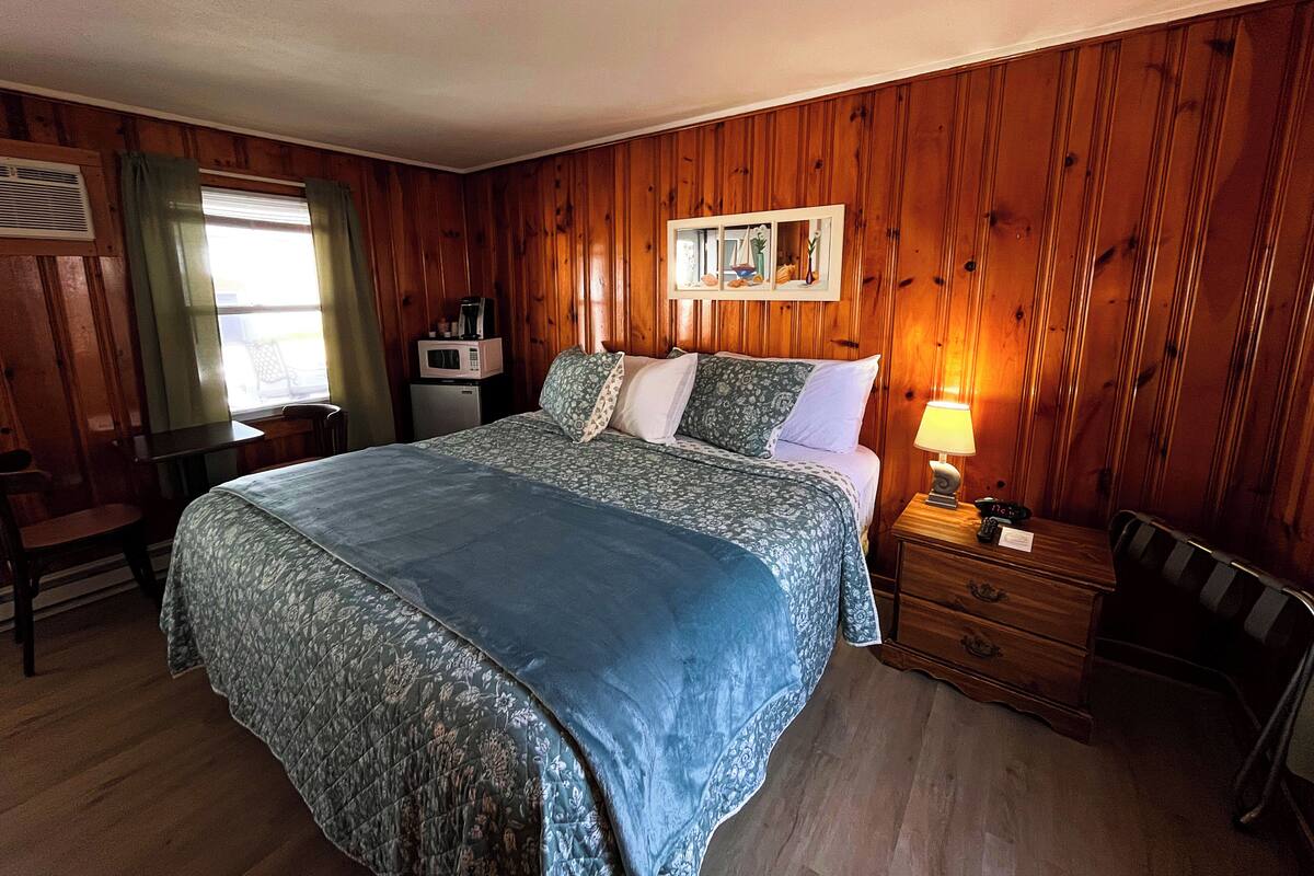 A room with a bed, a desk, a chair, a lamp, and a picture frame on the wall.