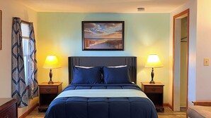 Une chambre à coucher avec un grand lit, deux tables de chevet avec des lampes, un tableau au-dessus du lit et un plancher en bois.
