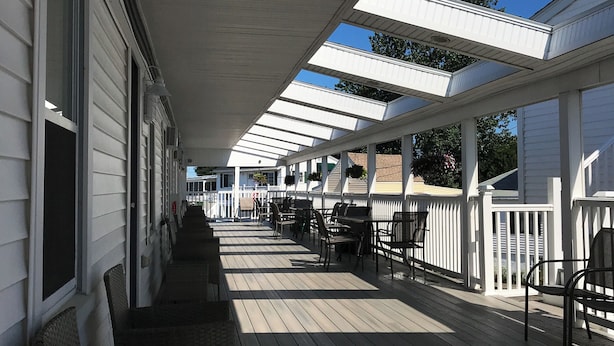 Un espace extérieur abrité doté d’une terrasse en bois, de rampes blanches et d’une série de fenêtres.