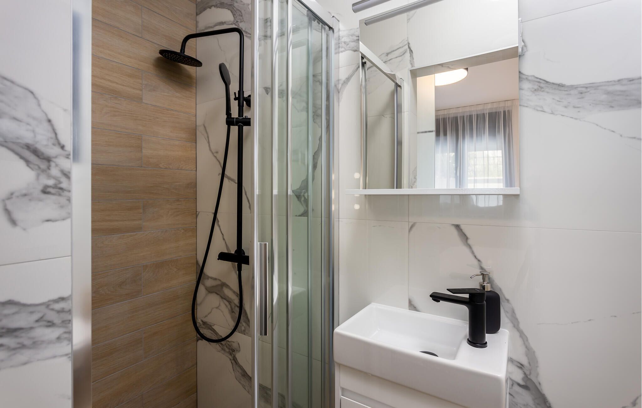 A modern bathroom with a glass-enclosed shower, a white sink, and marble walls.