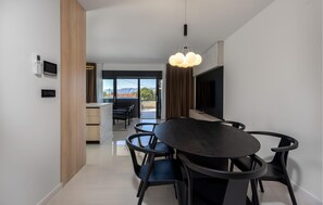 A modern dining area with a round table and chairs, a flat-screen TV mounted on the wall, and a view through the glass door. - 2 bedroom nice apartment in Novi Vinodolski (Novi Vinodolski)