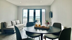 Ein modernes Wohnzimmer mit einer Couch, einem Esstisch mit Stühlen und einem großen Fenster mit Blick auf die Stadt.