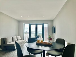 A modern living room with a sofa, a dining table with chairs, and a large window with a city view.