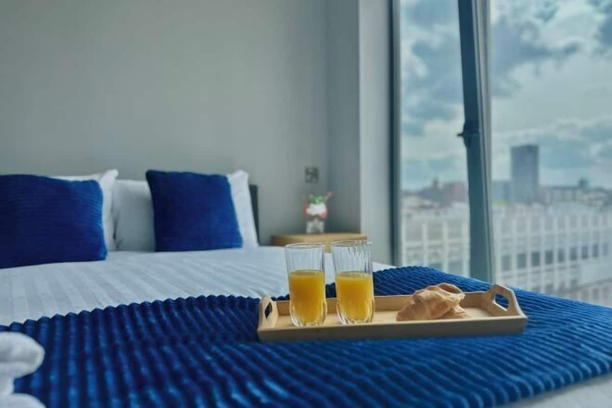 A hotel room with a bed, two glasses of orange juice, and a tray with a pastry on a blue bedspread.