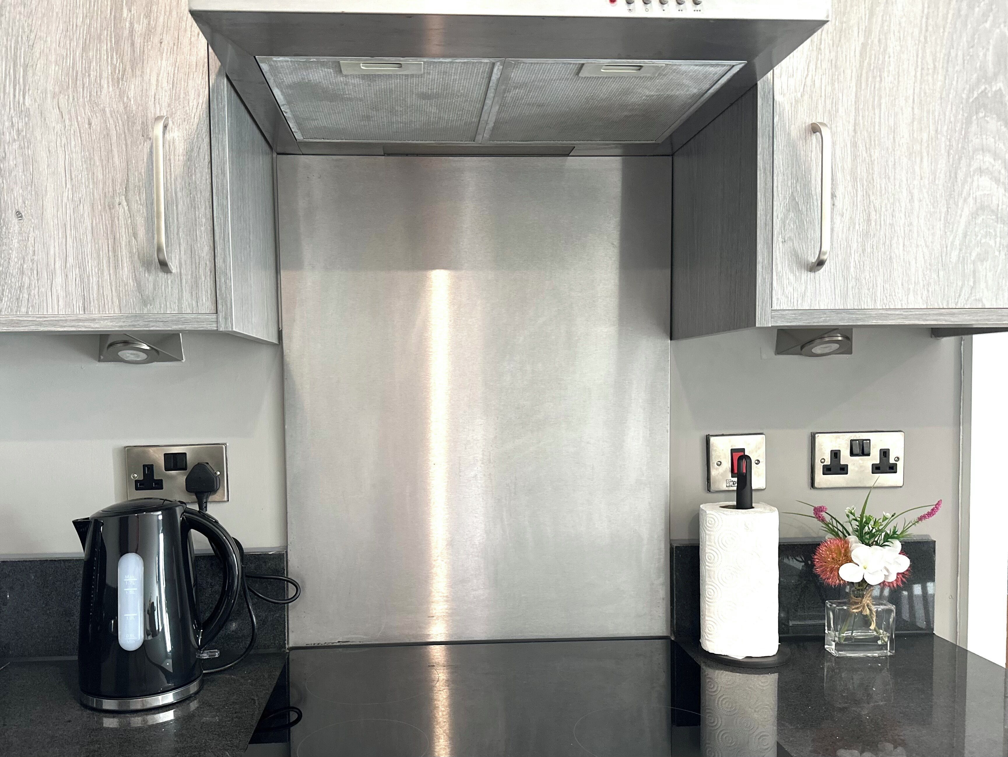 A kitchen with stainless steel appliances, a kettle, and a vase with flowers on the counter.