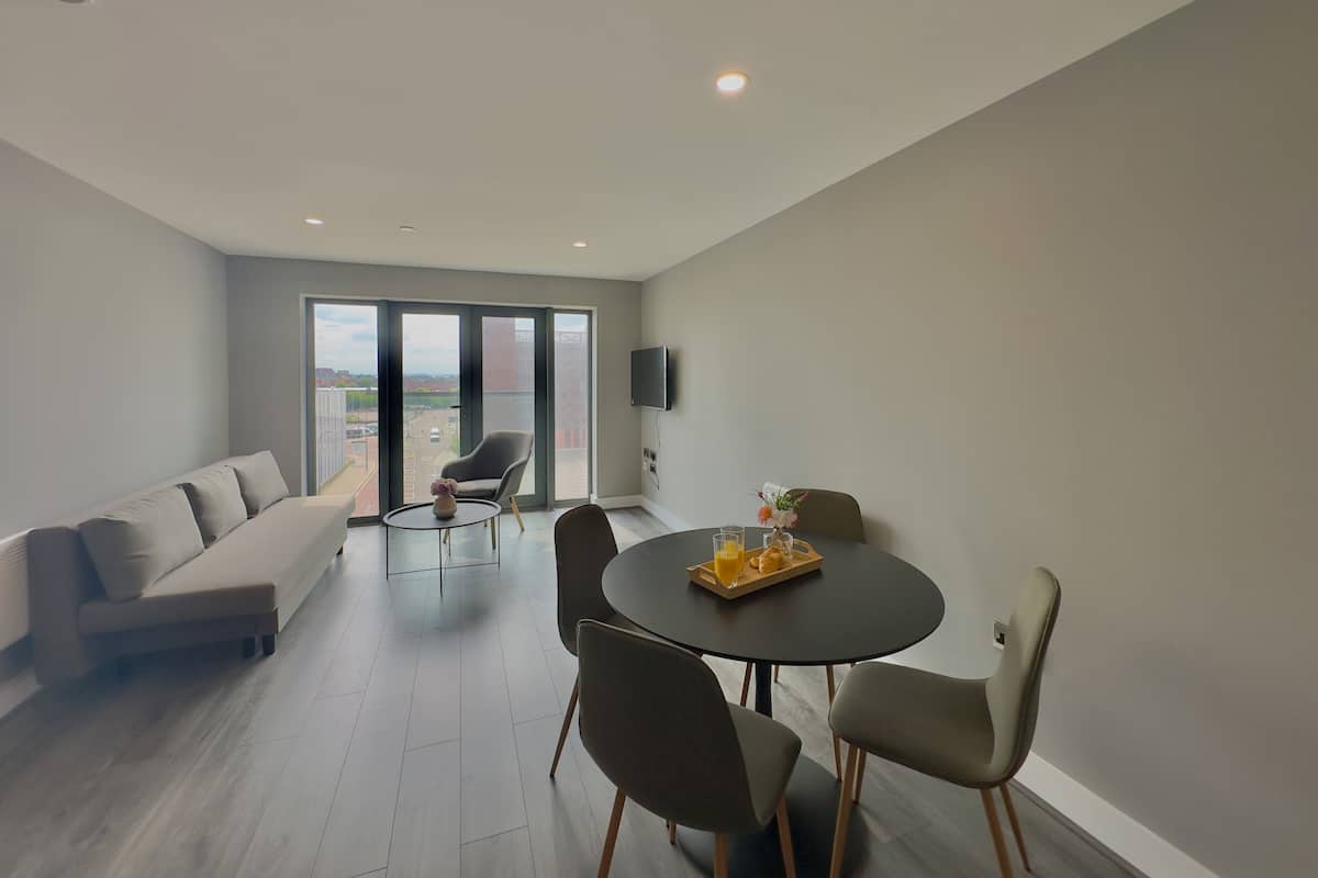 A modern living room with a sofa, a dining table with chairs, and a large sliding glass door leading to an outdoor balcony.