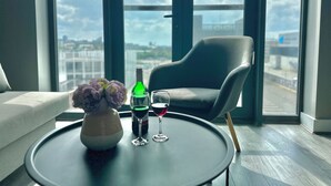 Ein modernes Zimmer mit einem großen Fenster, einem runden Tisch, einer Blumenvase, zwei Gläsern und einer Flasche.
