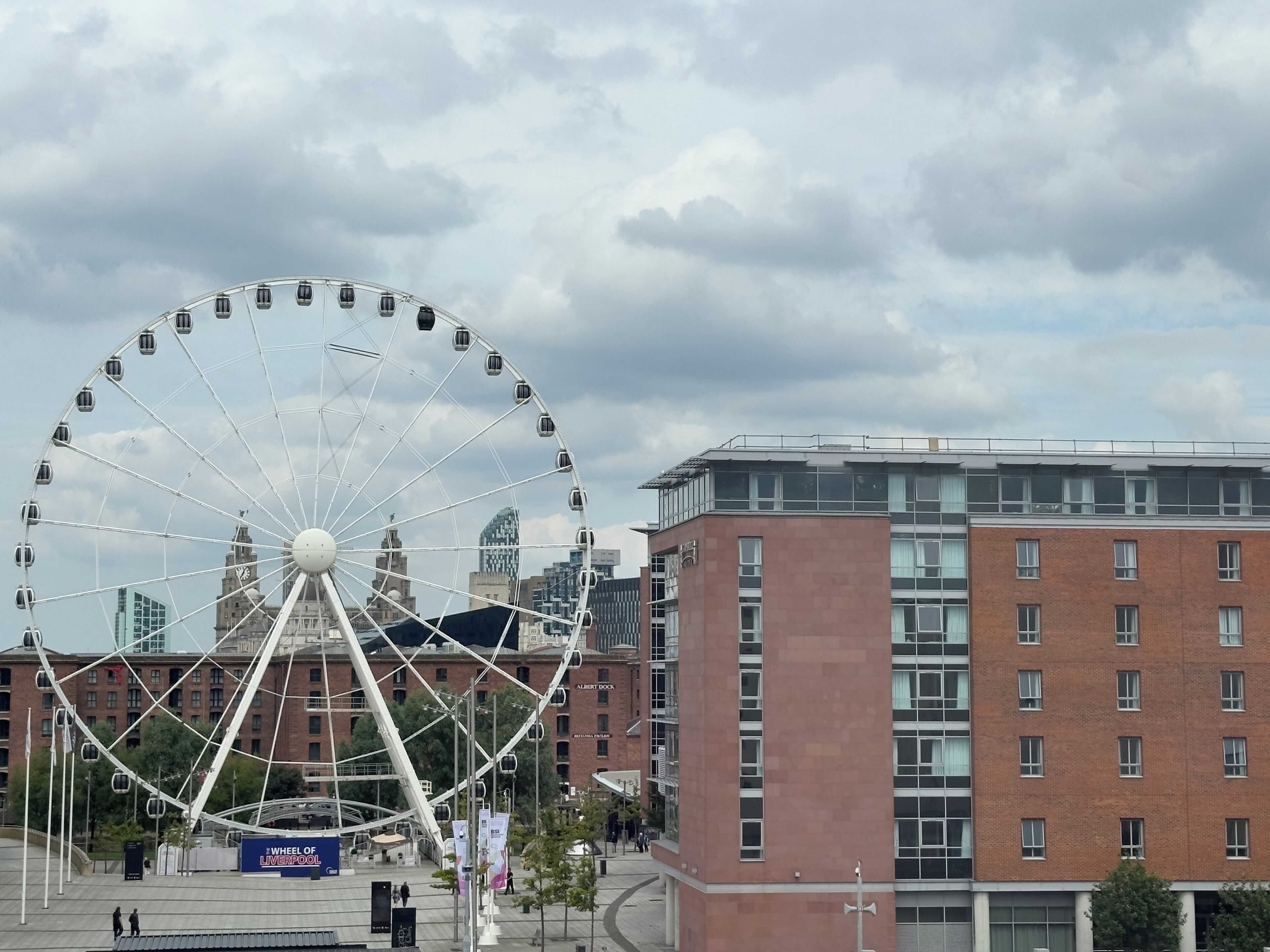 Une grande roue se dresse au milieu d’un paysage urbain, avec des bâtiments modernes en arrière-plan.