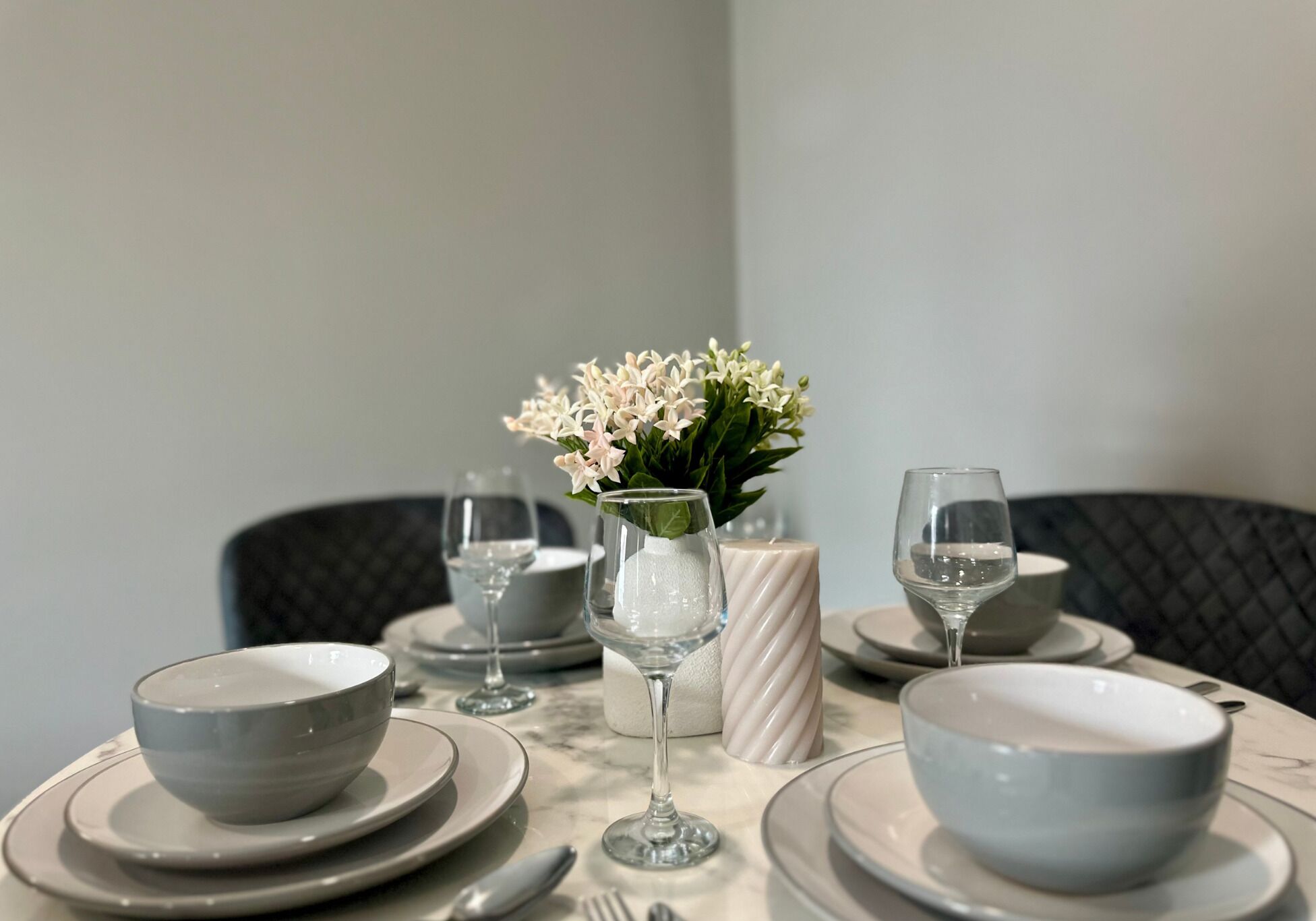 A dining table set with white plates, bowls, and wine glasses, accompanied by a vase of white flowers.