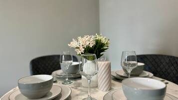 A dining table set with white plates, bowls, and wine glasses, accompanied by a vase of white flowers.