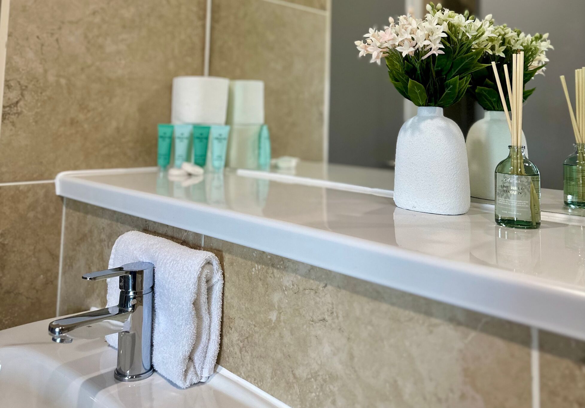 Ein Badezimmer mit Waschbecken, Handtuch, Spiegel und Toilettenartikeln auf der Ablagefläche.
