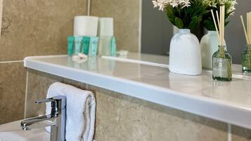 Ein Badezimmer mit Waschbecken, Handtuch, Spiegel und Toilettenartikeln auf der Ablagefläche.