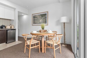 A modern kitchen with a dining area, featuring a round wooden table, beige chairs, and a decorative wall piece.