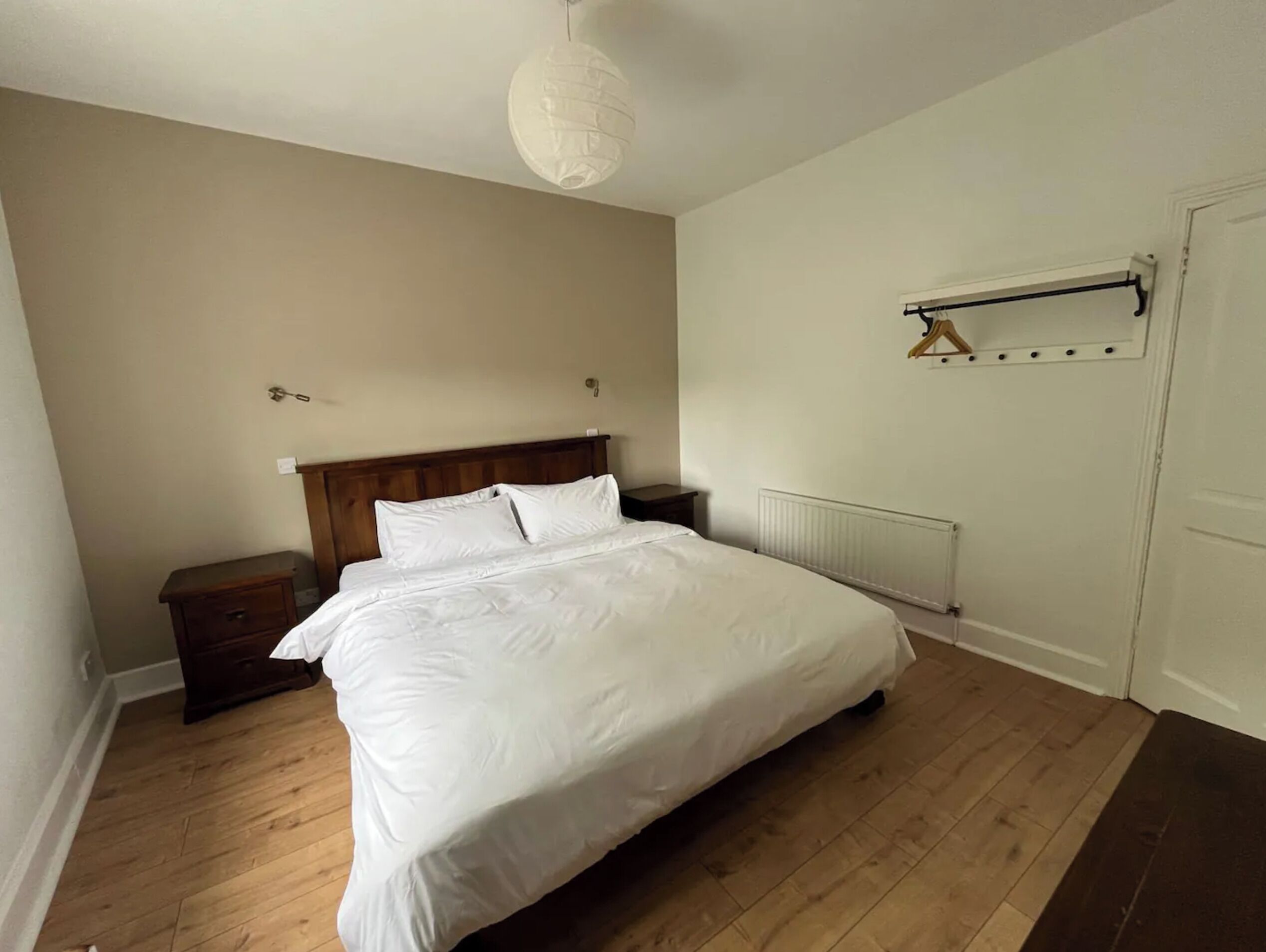 A bedroom with a wooden bed, a nightstand, a radiator, and a hanging light fixture.