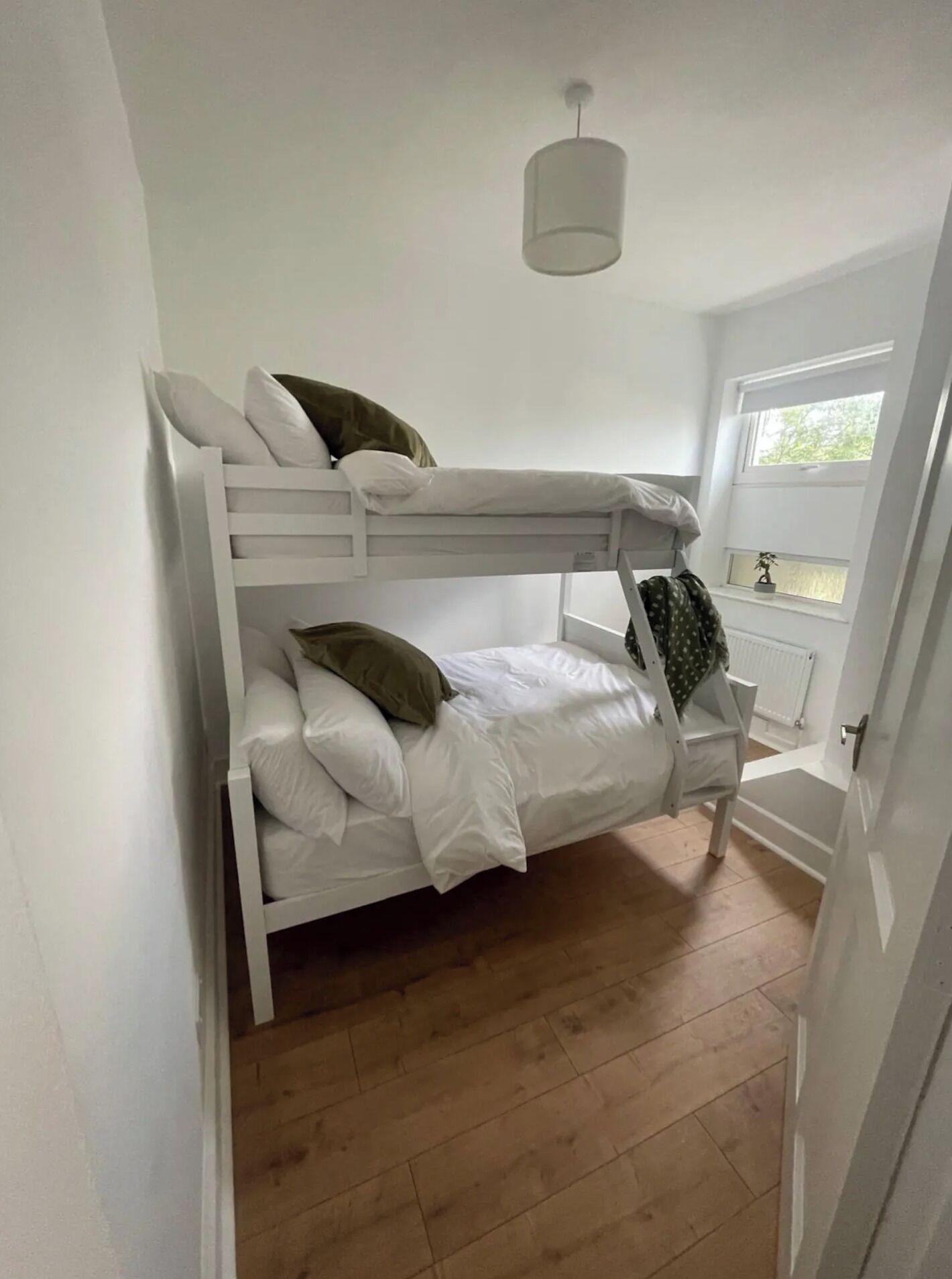 Dormitorio con literas, ropa de cama blanca, lámpara colgante y ventana con vistas a zonas verdes.