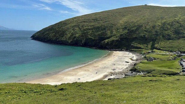 A coastal landscape with a beach, grassy areas, and a hill.