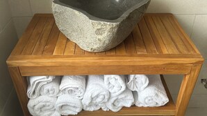 A wooden vanity with a stone sink, a shelf with folded towels, and wicker baskets.