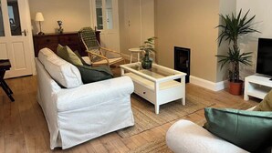 A living room with a sofa, armchair, coffee table, and a potted plant.