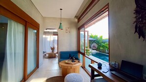 A modern room with a large window, a round wooden table, a blue sofa, and a laptop on a desk. - A private 200sqm entire villa, pool & rooftop with rice field view (Bali)
