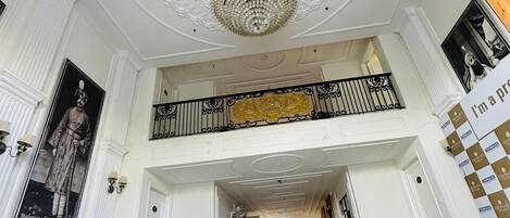 A grand lobby with a high ceiling, ornate ceiling design, and a chandelier.