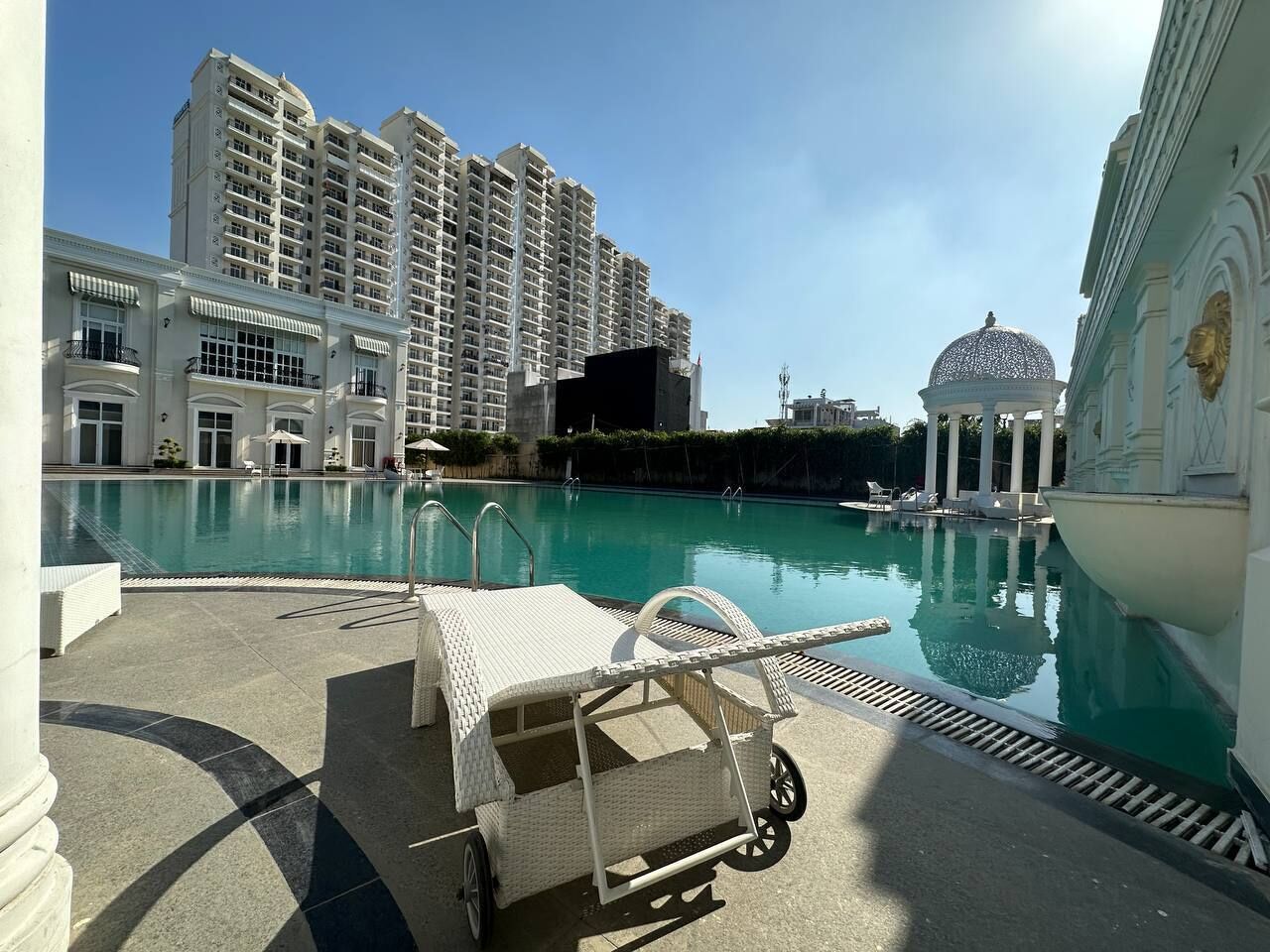 A pool area with a lounge chair and a cart, surrounded by high-rise buildings and a dome structure.