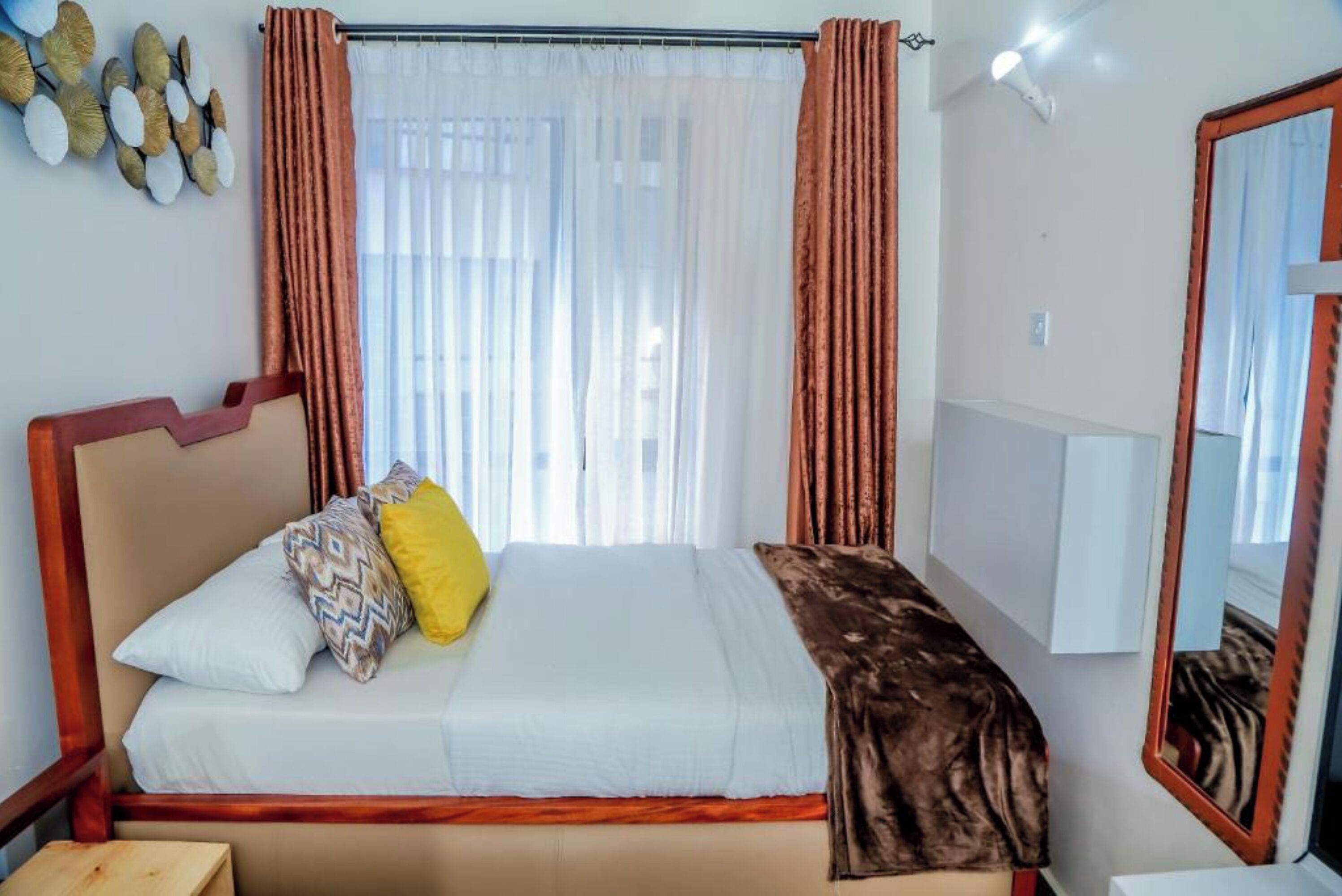 A bedroom with a bed, curtains, a mirror, and a wall decoration.