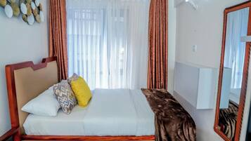 A bedroom with a bed, curtains, a mirror, and a wall decoration.