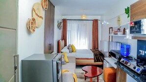 Een compacte hotelkamer met kitchenette, een bed met hoofdeinde, een tafeltje en een bank.