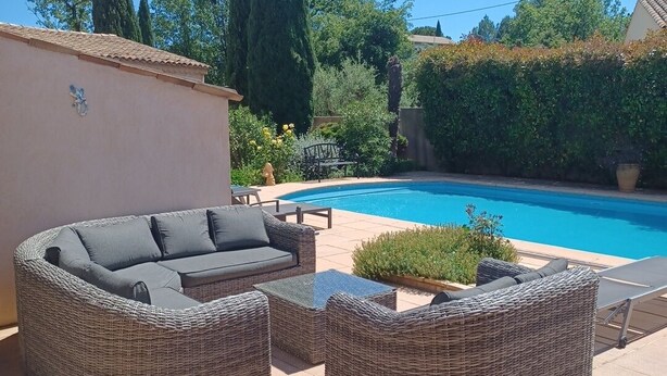 Un área junto a la piscina con mobiliario de mimbre, una pequeña mesa y un banco.