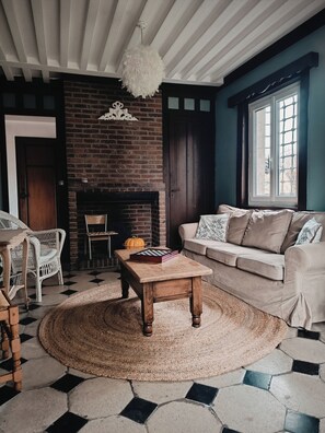 A living room with a brick fireplace, a round wooden coffee table, a beige sofa, and a white wicker chair.