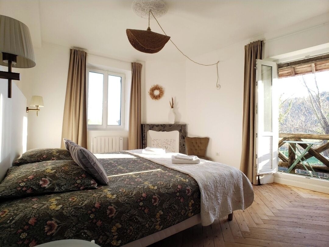 Une chambre à coucher avec un lit, une fenêtre, une vue sur les arbres, un plancher en bois et un luminaire au plafond.