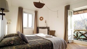 Un dormitorio con cama, ventana, vistas a árboles, suelo de madera y lámpara en el techo.