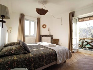 Une chambre à coucher avec un lit, une fenêtre, une vue sur les arbres, un plancher en bois et un luminaire au plafond.
