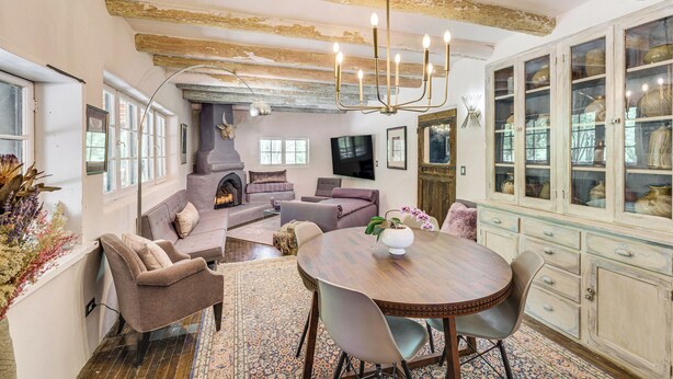 A spacious living room with a fireplace, comfortable seating, a dining area with a round table, and a kitchen with glass-front cabinets. - Mid-century Modern Taos Home w/ Hot Tub & Fire Pit (Taos)