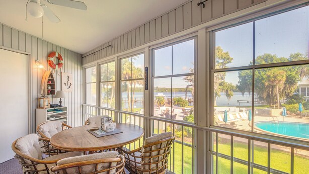 A sunlit room with a large window overlooking a swimming pool, wicker furniture, and a ceiling fan. - Pool Access & Lanai: Riverfront Welaka Condo! (Welaka)