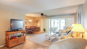 A living room with a television, wicker furniture, a dining area, and a large window. - Pool Access & Lanai: Riverfront Welaka Condo! (Welaka)