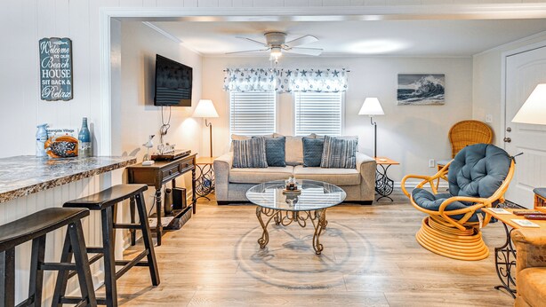 A living room with a wooden floor, a glass coffee table, a sofa, a chair, and a bar area with stools. - 1/2 Mi to Ocean: Surfside Beach Resort Home (Murrells Inlet)