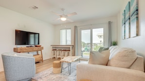 A modern living room with a flat-screen TV, a sofa, a coffee table, and a dining area with a wooden table and chairs. - Beachy Gulf Shores Condo w/ Pool, Walk to Shore! (Gulf Shores)