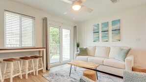 A living room with a sofa, a coffee table, and a set of bar stools. - Beachy Gulf Shores Condo w/ Pool, Walk to Shore! (Gulf Shores)