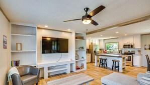A modern living room with a flat-screen TV, built-in shelves, a grey sofa, a wooden coffee table, and a ceiling fan. - Cedar Creek Reservoir Home w/ Private Boat Ramp! (Kemp)