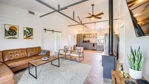 A spacious living room with a brown leather sofa, wooden chairs, a coffee table, and a large plant. - Peaceful Vinita Home w/ Fire Pit: 11 Mi to Lake! (Vinita)