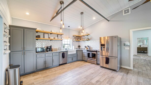 A modern kitchen with grey cabinets, stainless steel appliances, wooden flooring, and pendant lighting. - Peaceful Vinita Home w/ Fire Pit: 11 Mi to Lake! (Vinita)